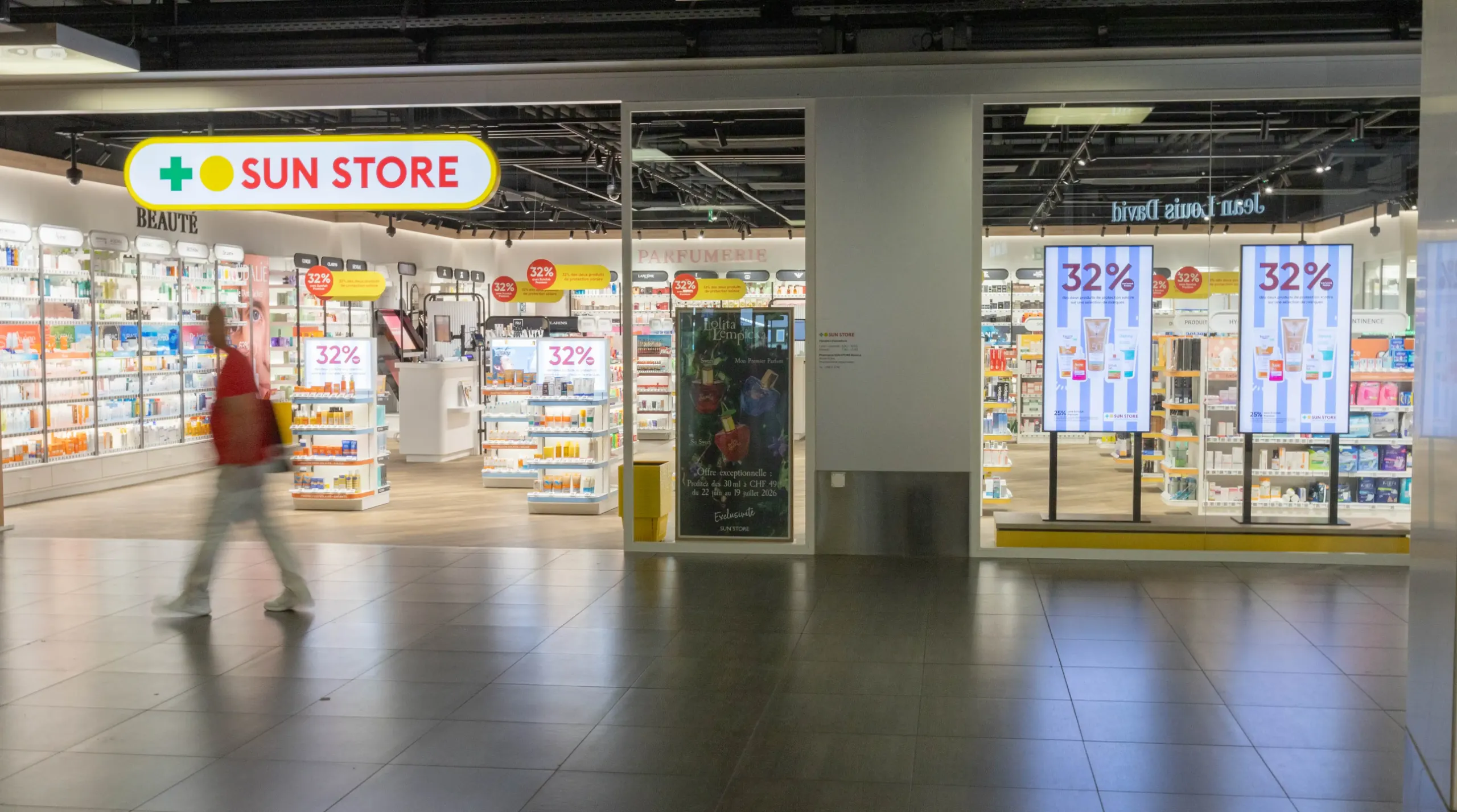 Sun Store Filiale mit beidseitig montierten Digital-Signage-Screens im Gang, Kundschaft läuft vorbei